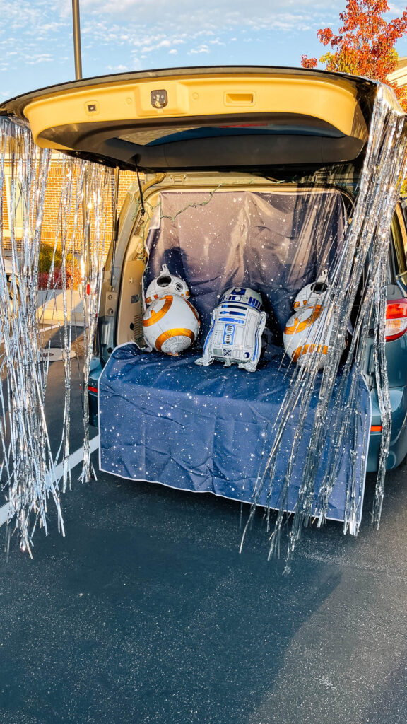 Open trunk with silver door curtains, space backdrop and droid balloons.