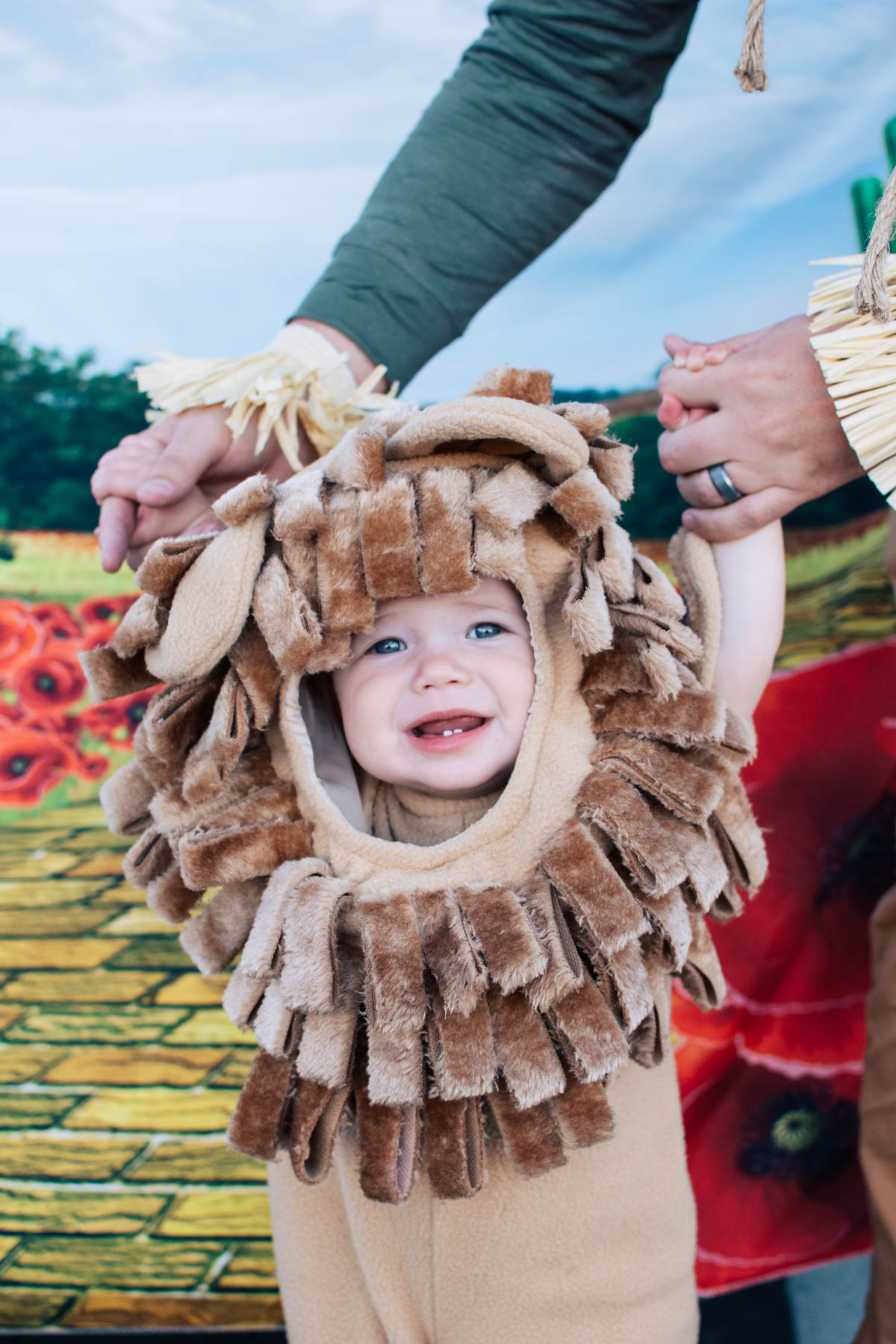 Man holds baby girl wearing Cowardly Lion costume in front of yellow brick road.
