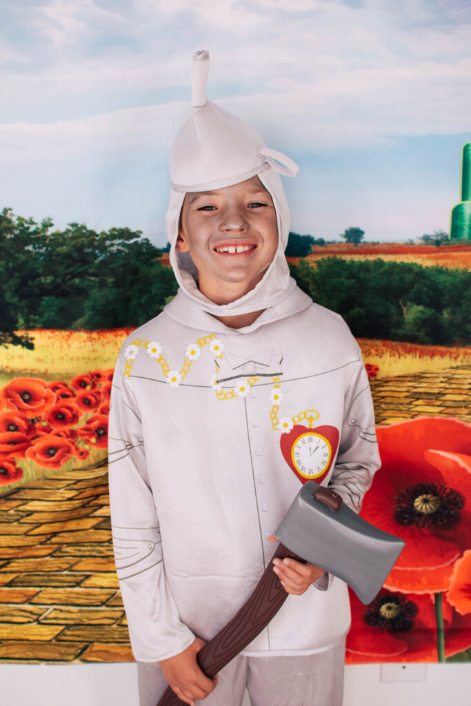 Boy dressed as the Tin Man holds ax in front of yellow brick road.