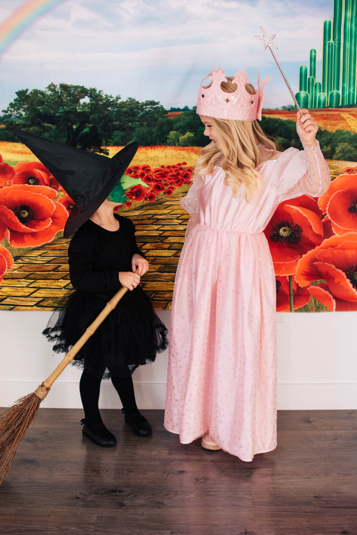 Two sisters dressed as the Wicked Witch and Glinda smile at each other.