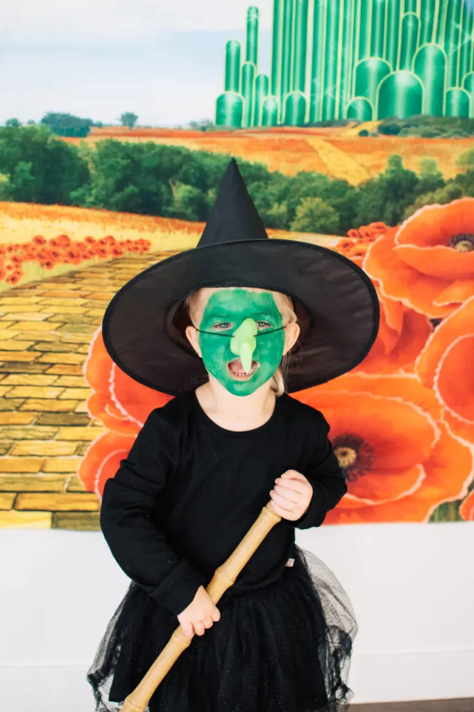 Girl dressed as Wicked Witch scowls while holding broom.
