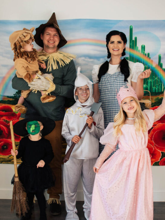 Family of 6 dressed as Wizard of Oz characters pose in front of Emerald city backdrop.