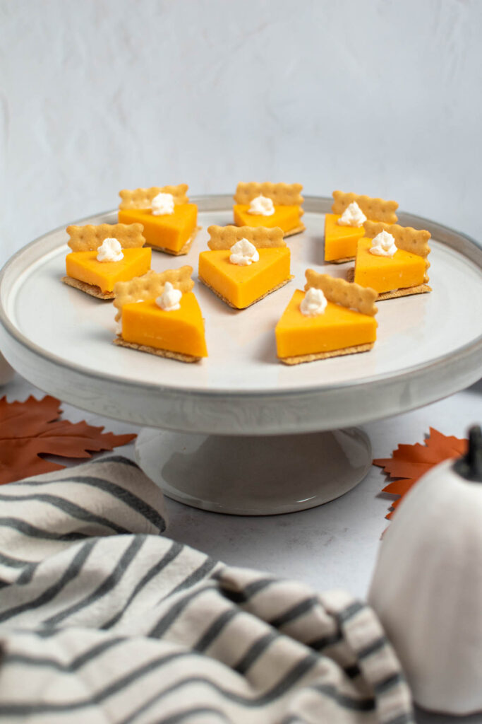 Cheese and cracker pumpkin pie bites on off white cake stand.