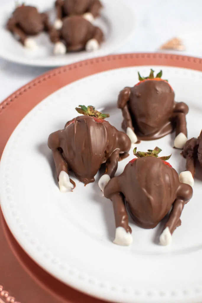 Three chocolate covered strawberries that look like turkeys on white plate.