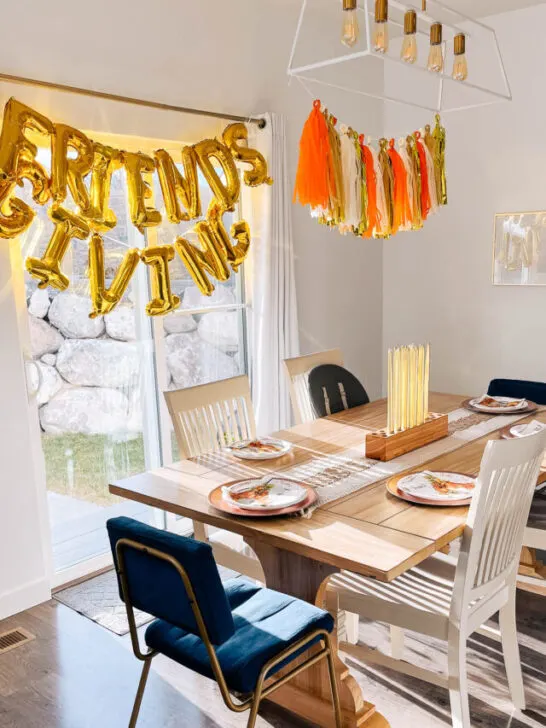 Dinner table decorated for friendsgiving with a tassel garland and balloon banner nearby.