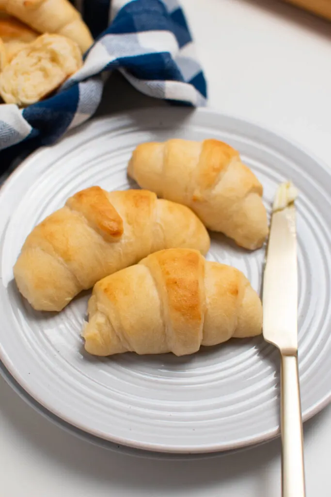 Three crescent rolls on white plate with butter knife resting nearby.
