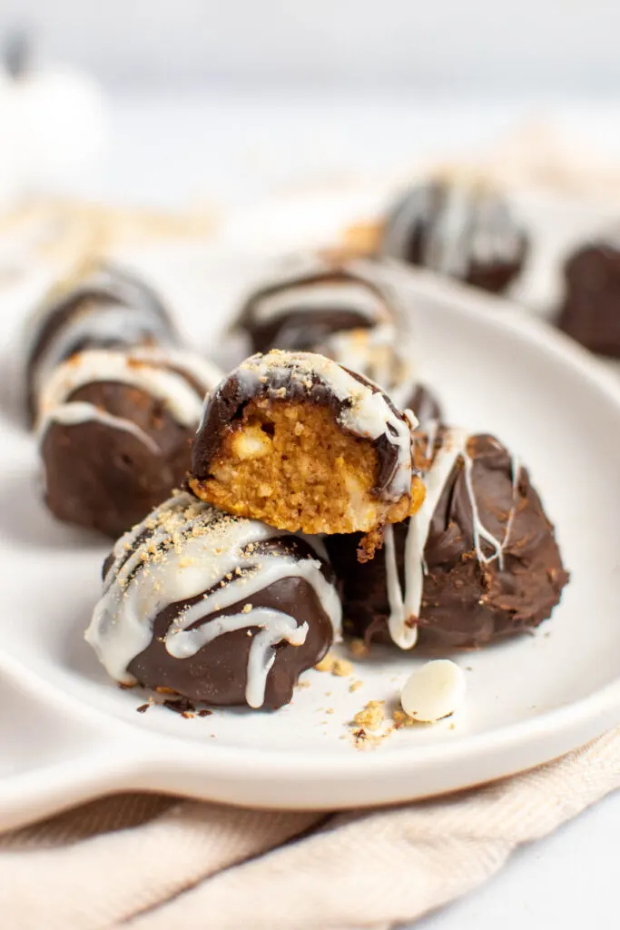 Stack of pumpkin pie truffles with one cut in half on white plate.