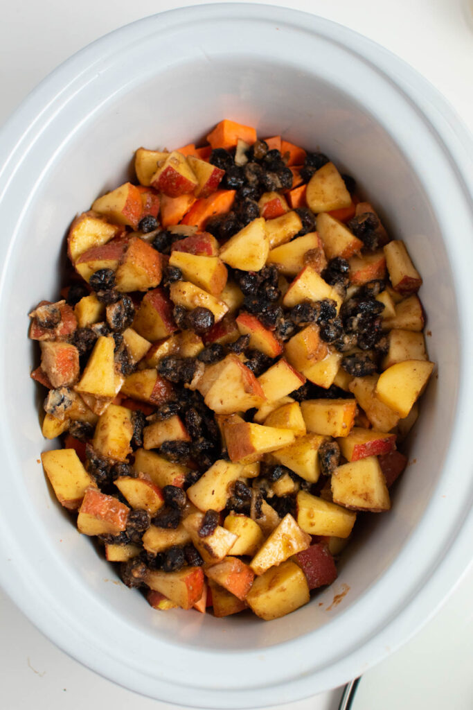 White Crock Pot insert full of sweet potatoes, apples, and dried cranberries.
