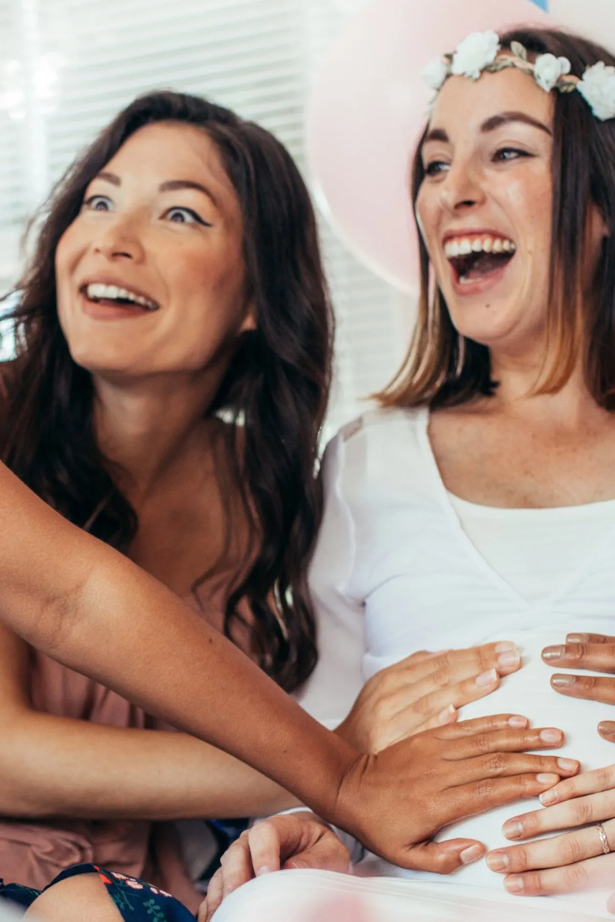 A pregnant woman and her baby shower guests touch her belly with excited faces.