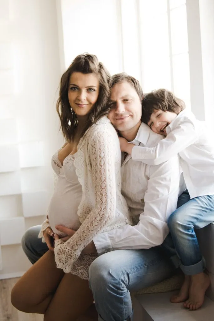 A pregnant woman poses with her husband and son in front of a window.