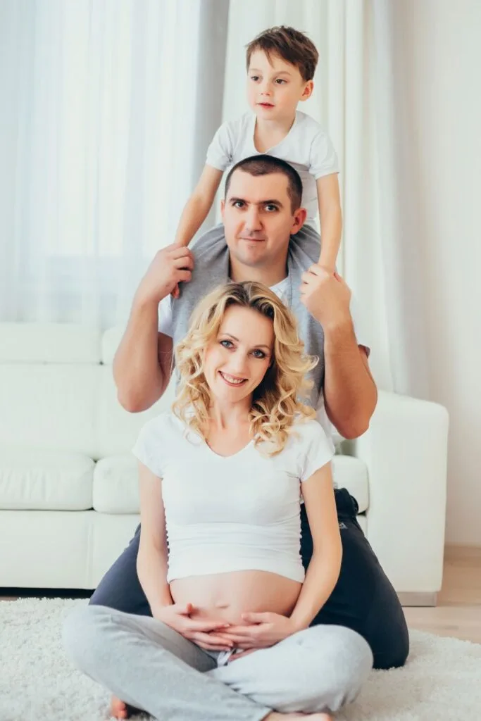 A pregnant woman poses with her family in front of a white couch.