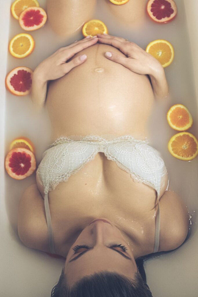 A pregnant woman poses in a milk bath with slices of citrus fruits.