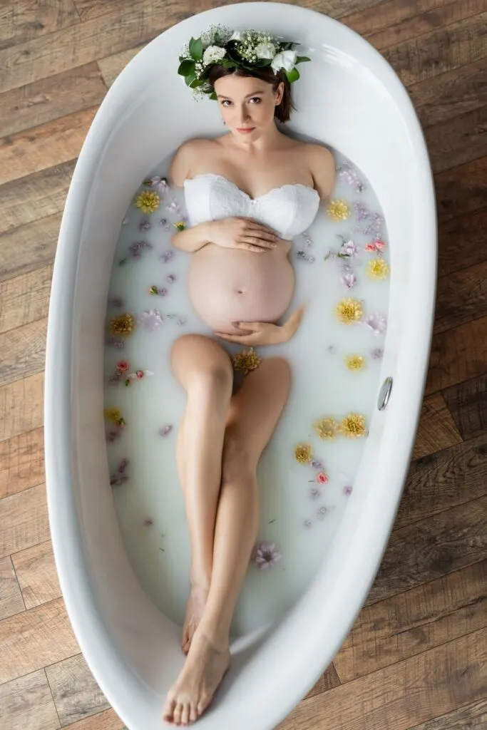 A pregnant woman poses in a milk bath with while wearing a flower crown.