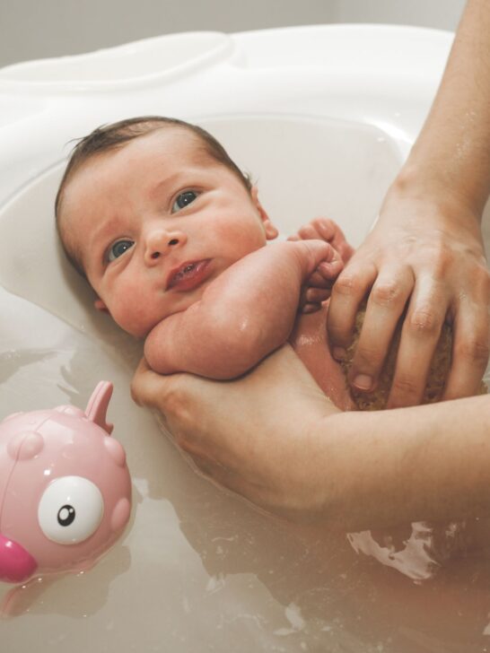 A baby is rubbed with a sponge in a small white bathtub.