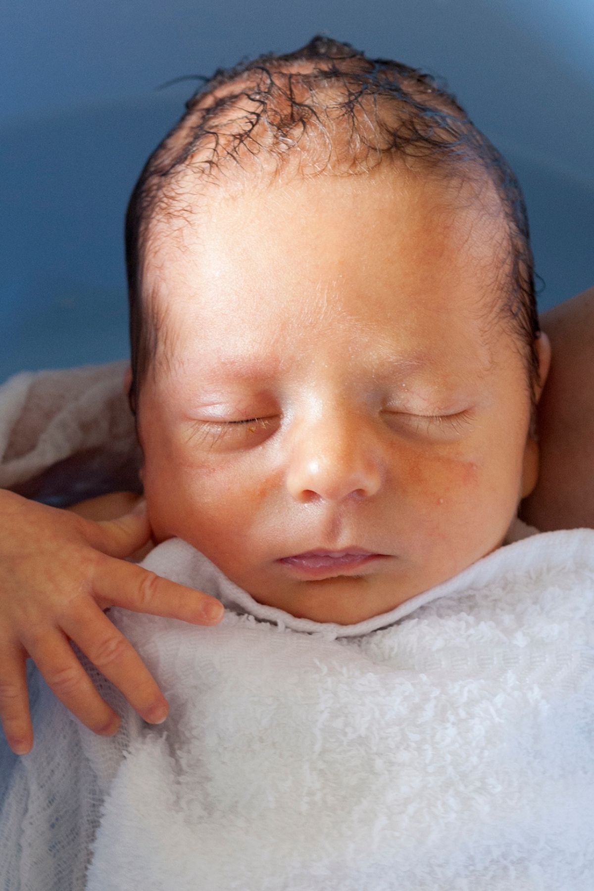 A newborn getting a bath with a white cloth over their chest.