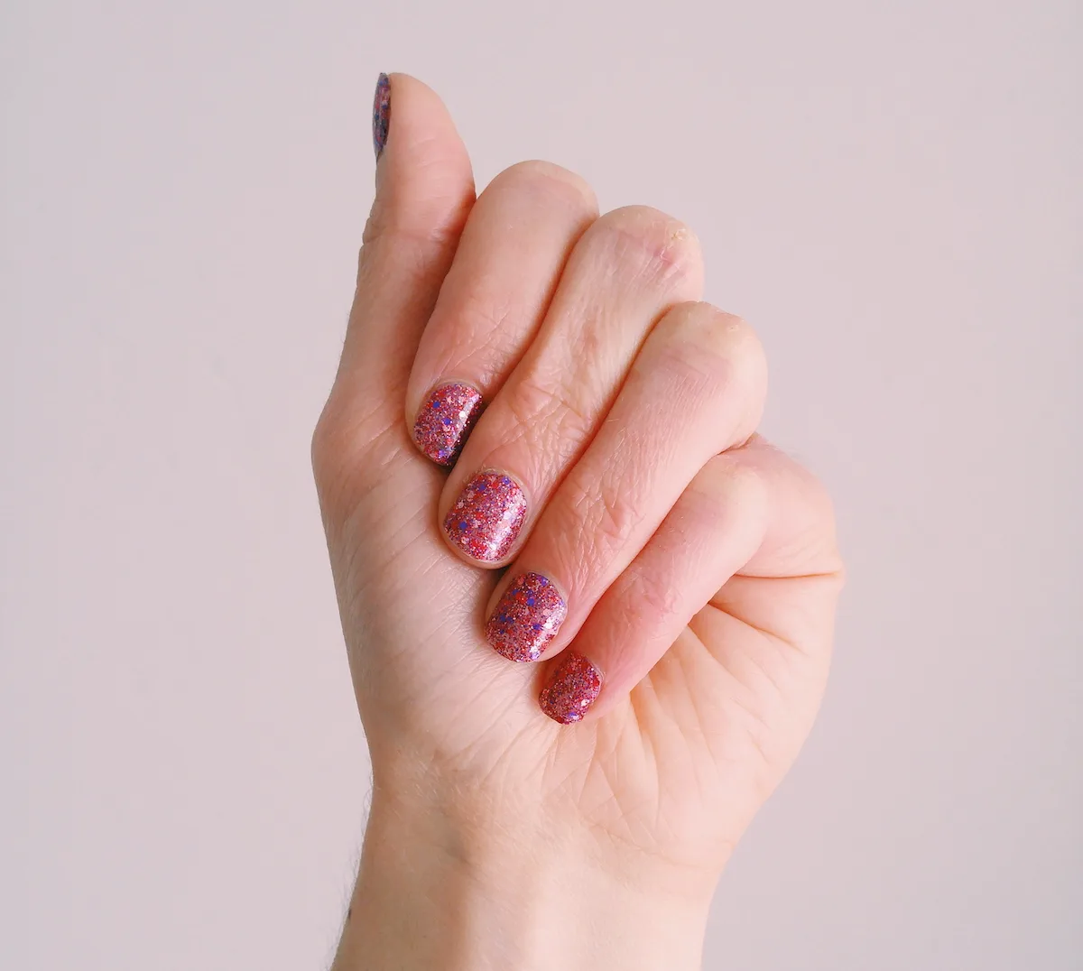 Woman's hand showing pink and purple glitter nails.