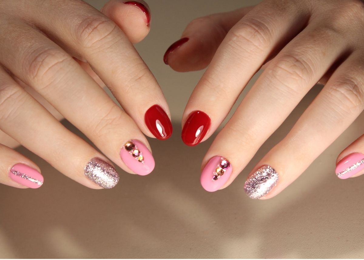 Red, pink, and silver painted fingernails with a jewel design on the nails painted pink.