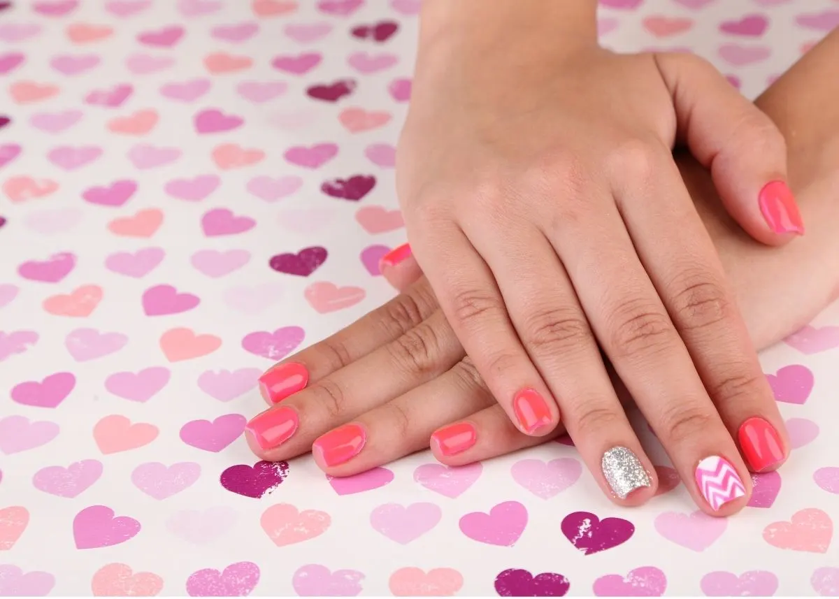 Crossed hands rest on a Valentine's Day background with fingernails painted pink and silver.