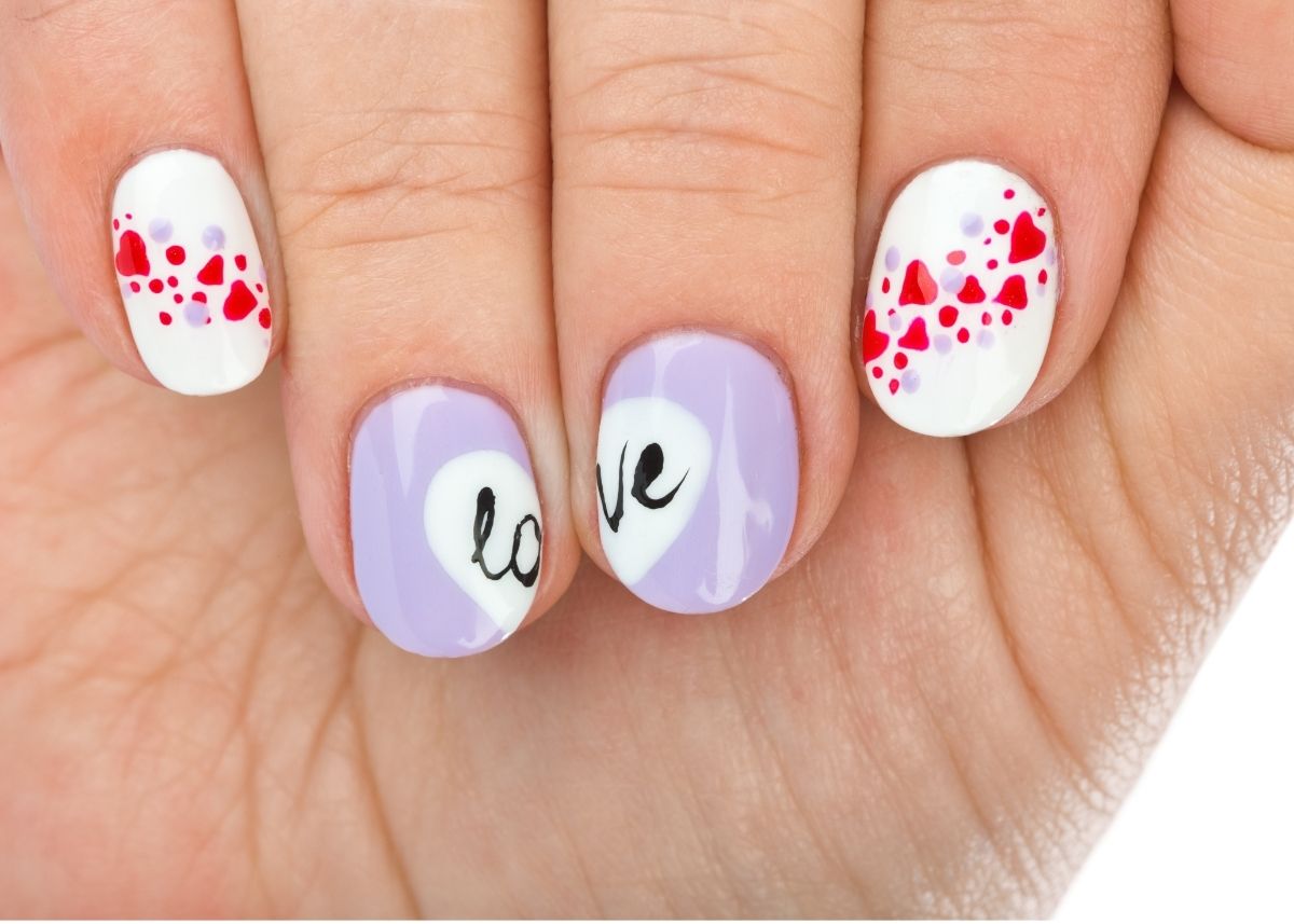 A cupped hand shows fingernails painted for Valentine's Day with two outer fingers painted white with miniature red hearts and two fingers in the middle painted purple with the word "love" spelled between the two fingers.