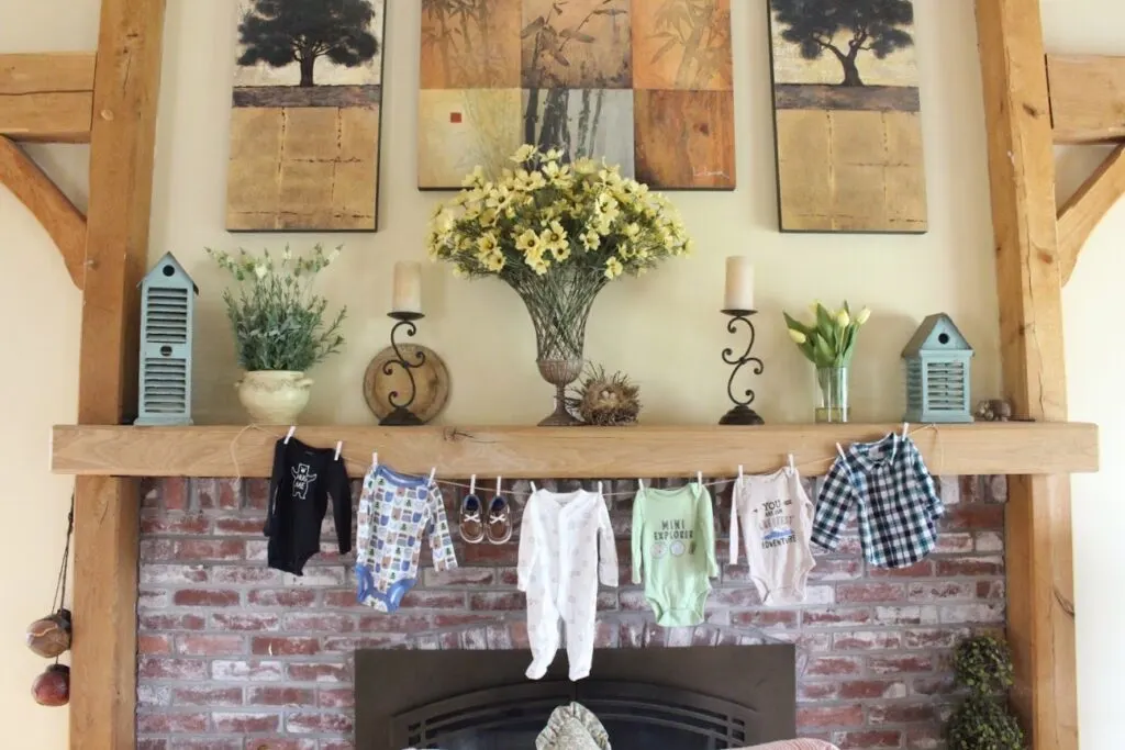 Green, white, and blue onesies for a baby boy hang from a clothesline in front of a fireplace.