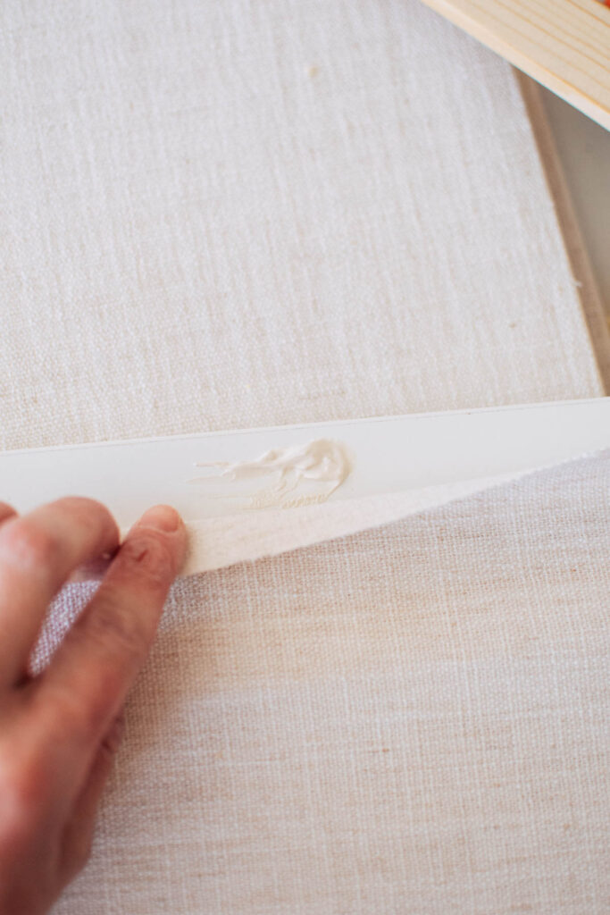 Woman pulls back linen fabric to show glob of wood glue on white wood.