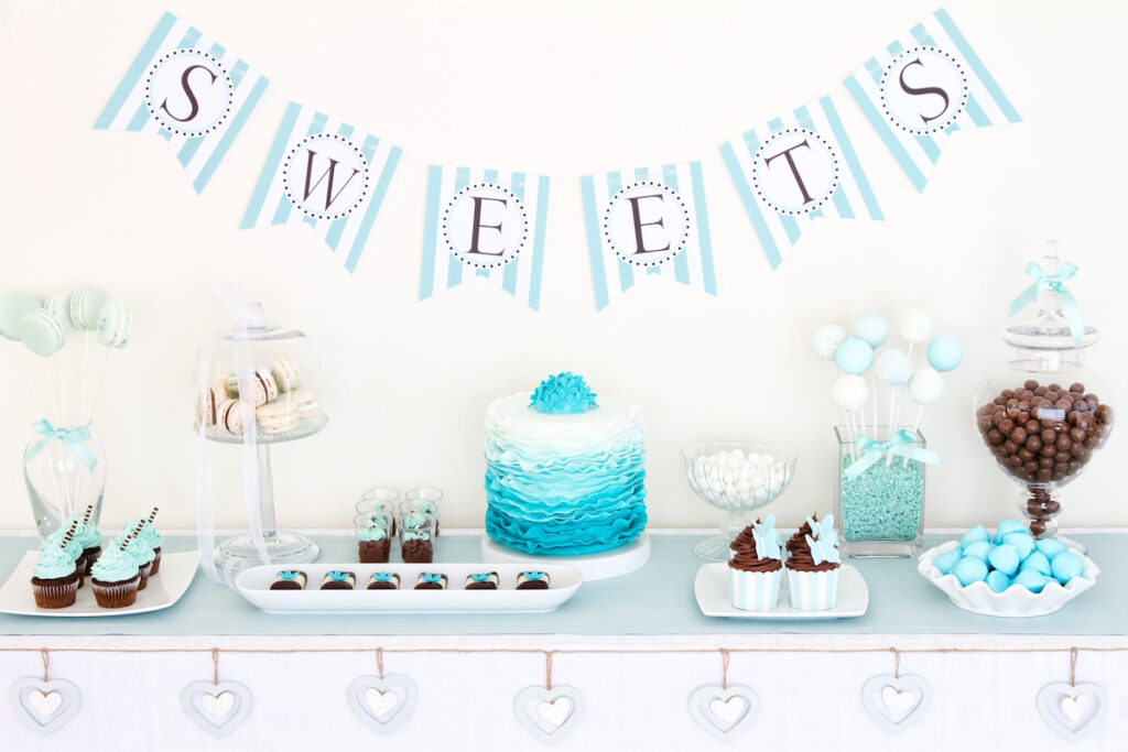 Dessert table with blue and whites sweets including a cake, cupcakes, cakepops, and candies.