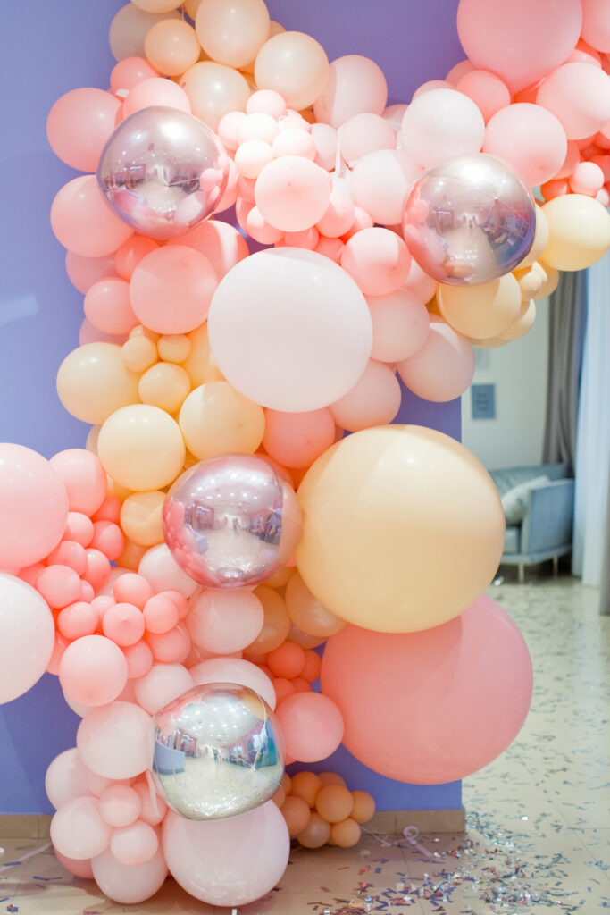 Pink, silver, and peach colored balloon garland hanging in front of purple background.