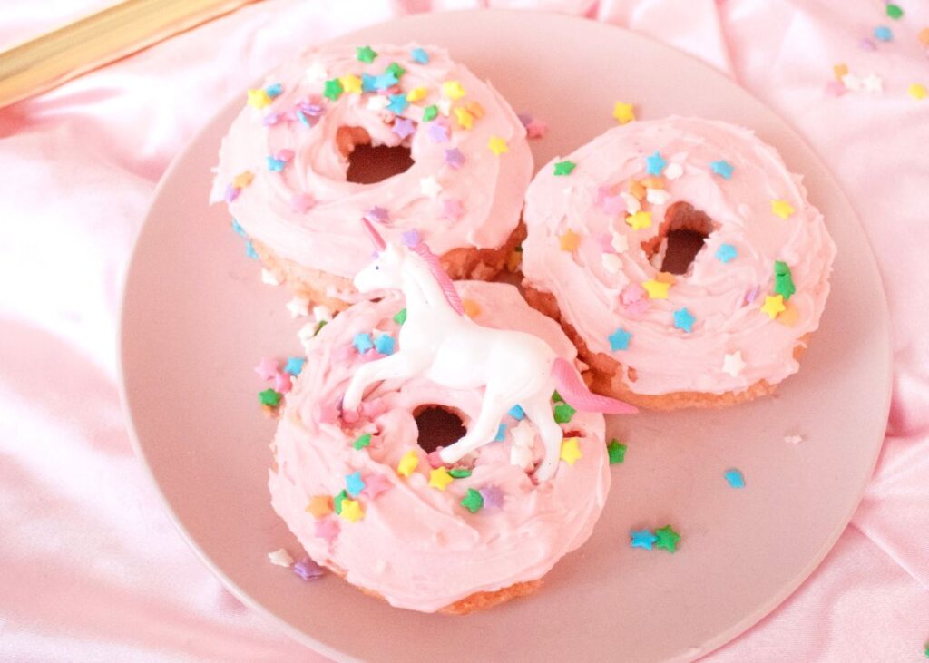 Donuts with pink icing, sprinkles, and a unicorn on a pink plate.