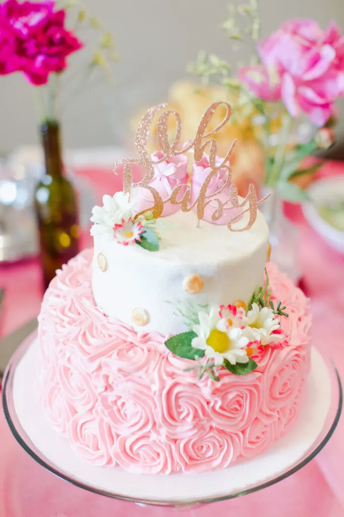 A pink and white floral cake with a cake topper that says "oh baby" on top.