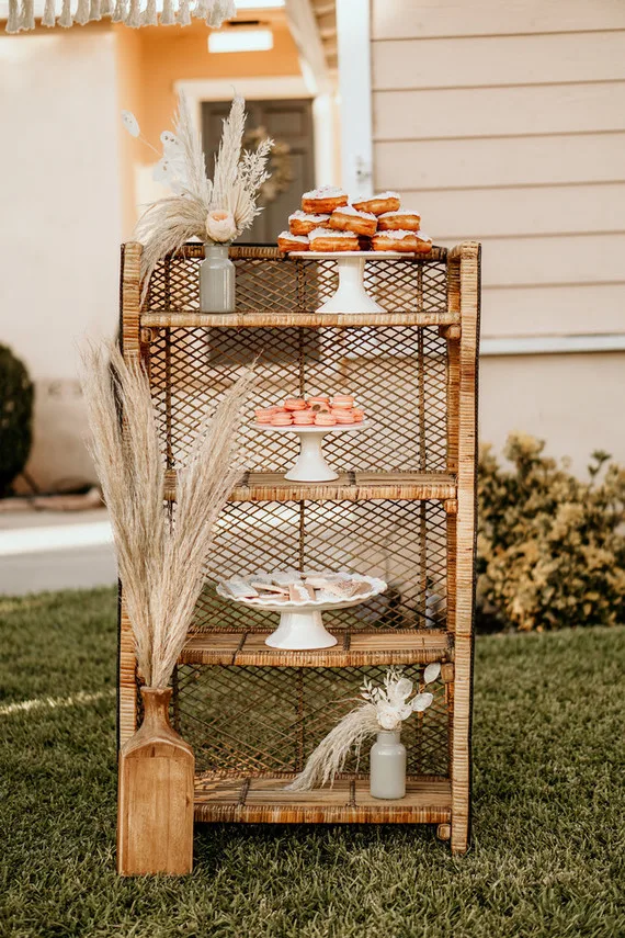A wicker shelf filled with desserts and boho decor outside.