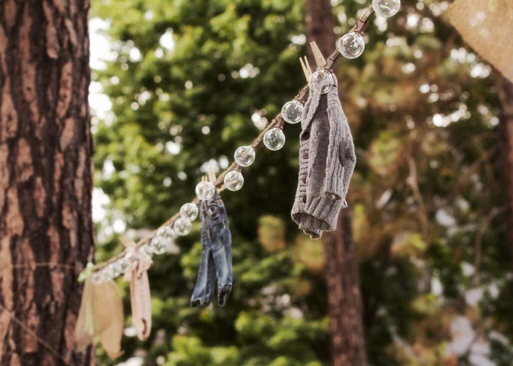 A string of lights hung between two trees with boy baby clothes.