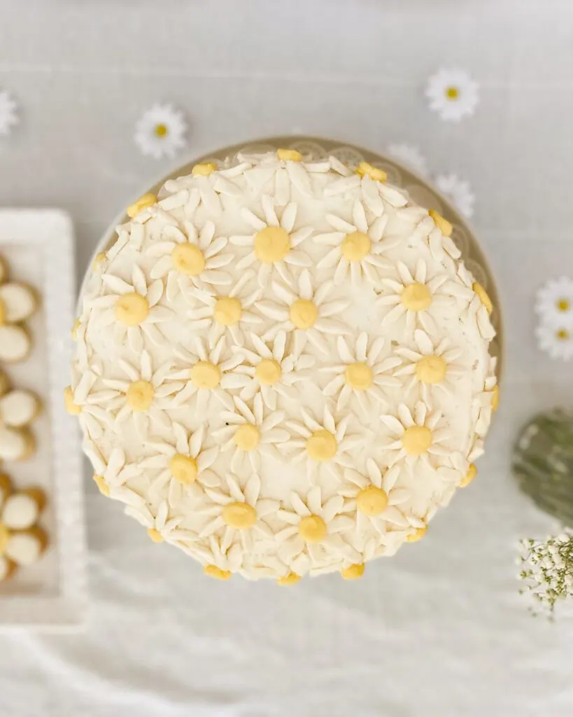 Over-head shot of a daisy-decorated baby shower cake on a dessert table.