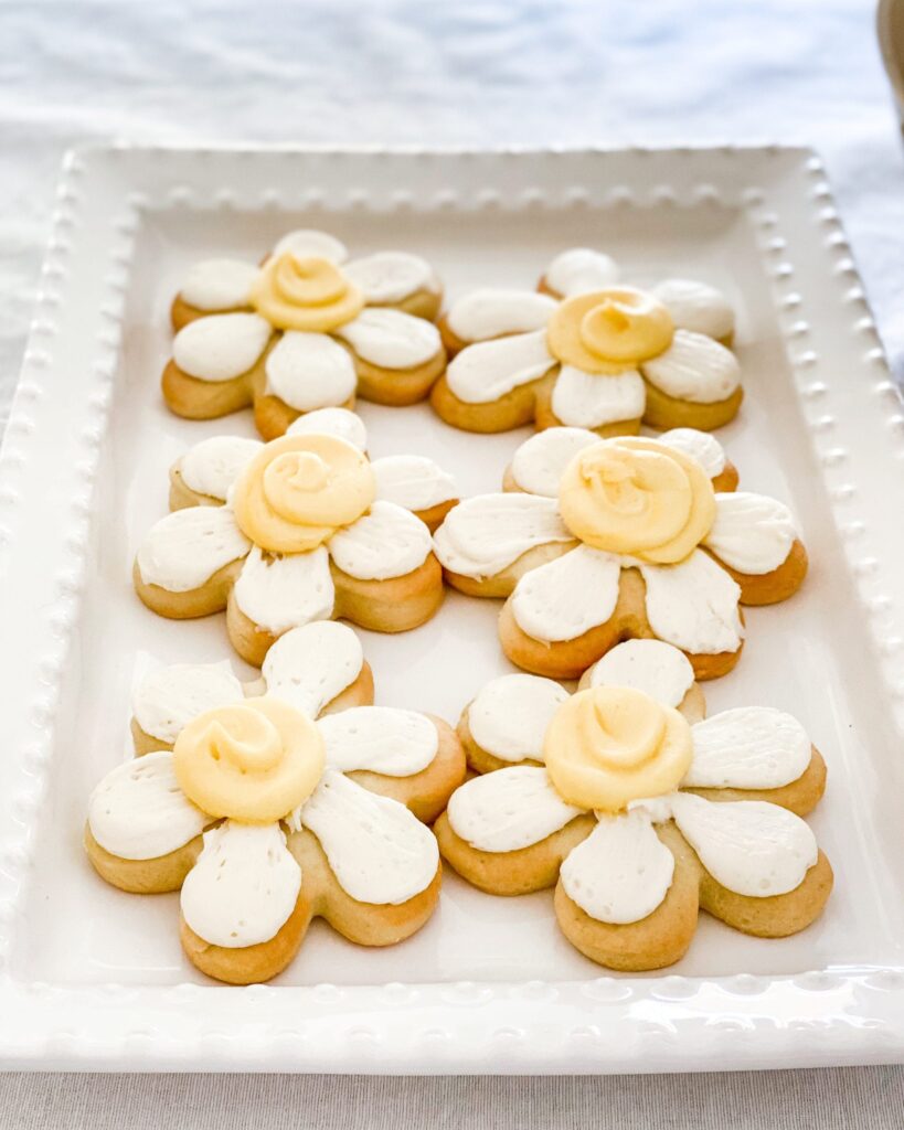 Daisy-shaped cookies with white and yellow icing on a white serving platter.