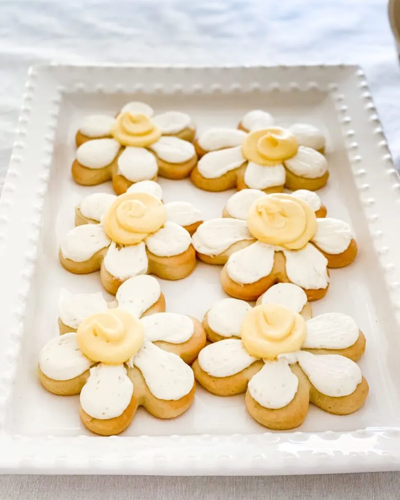 Daisy-shaped cookies with white and yellow icing on a white serving platter.