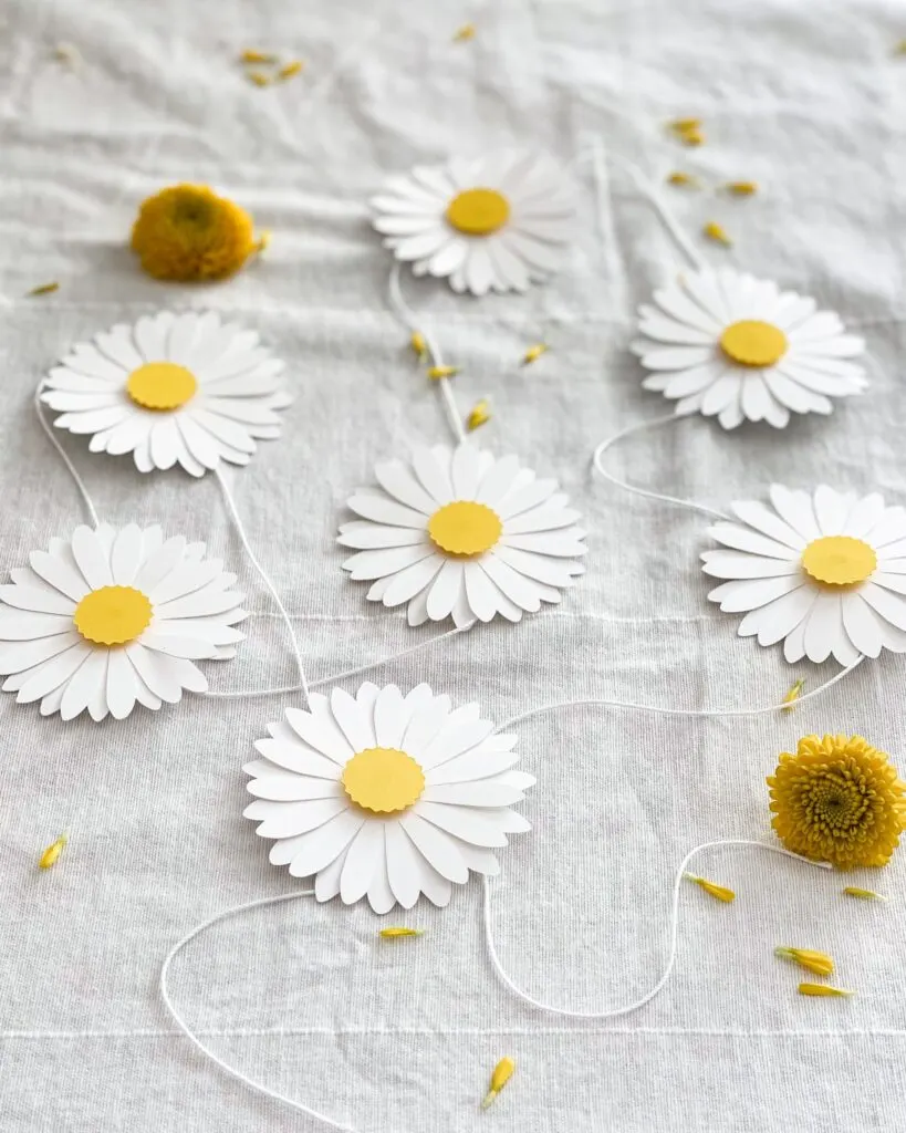 A paper daisy garland on a white tablecloth with real days flowers.