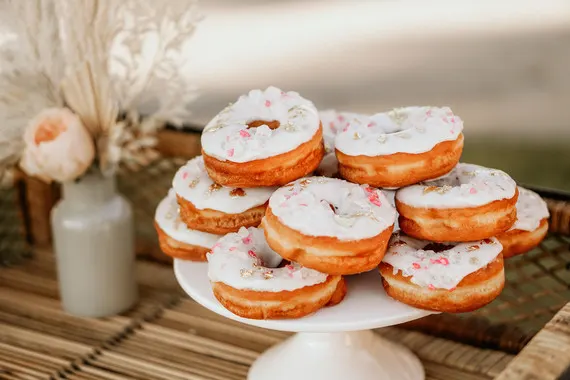 Donuts with white icing and sprinkles on a white cake stand.