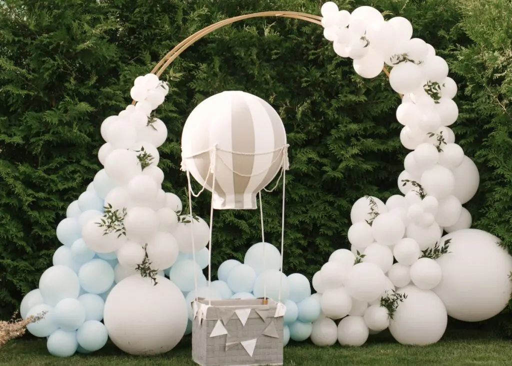 A gray, white, and blue balloon backdrop and a mini hot air balloon outside.