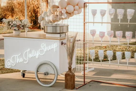 A cotton candy cart with cotton candy cones hanging on a stand and balloons.