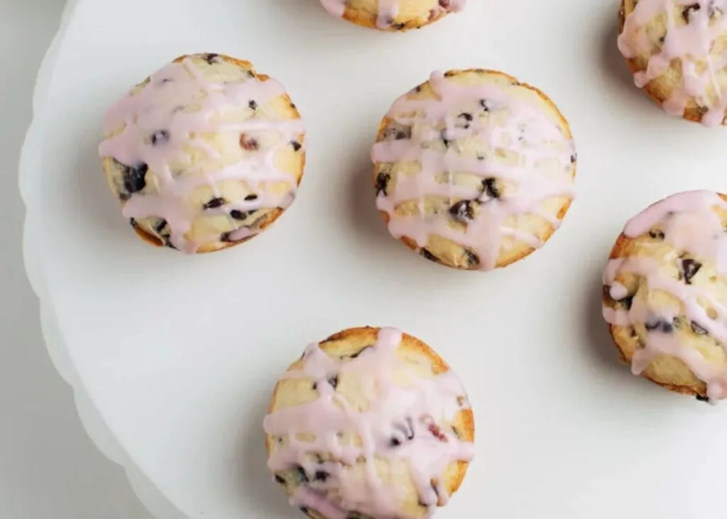 Cherry chip muffins with pink glaze on a white cake stand.