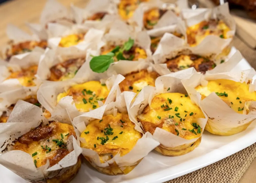 Mini quiches in white parchment paper on a white serving platter.