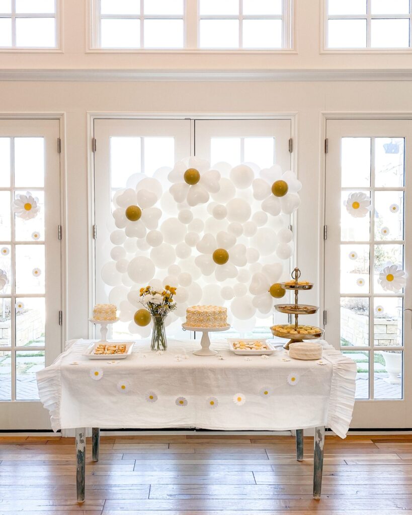 A food table with a white tablecloth and daisy balloons in the background,