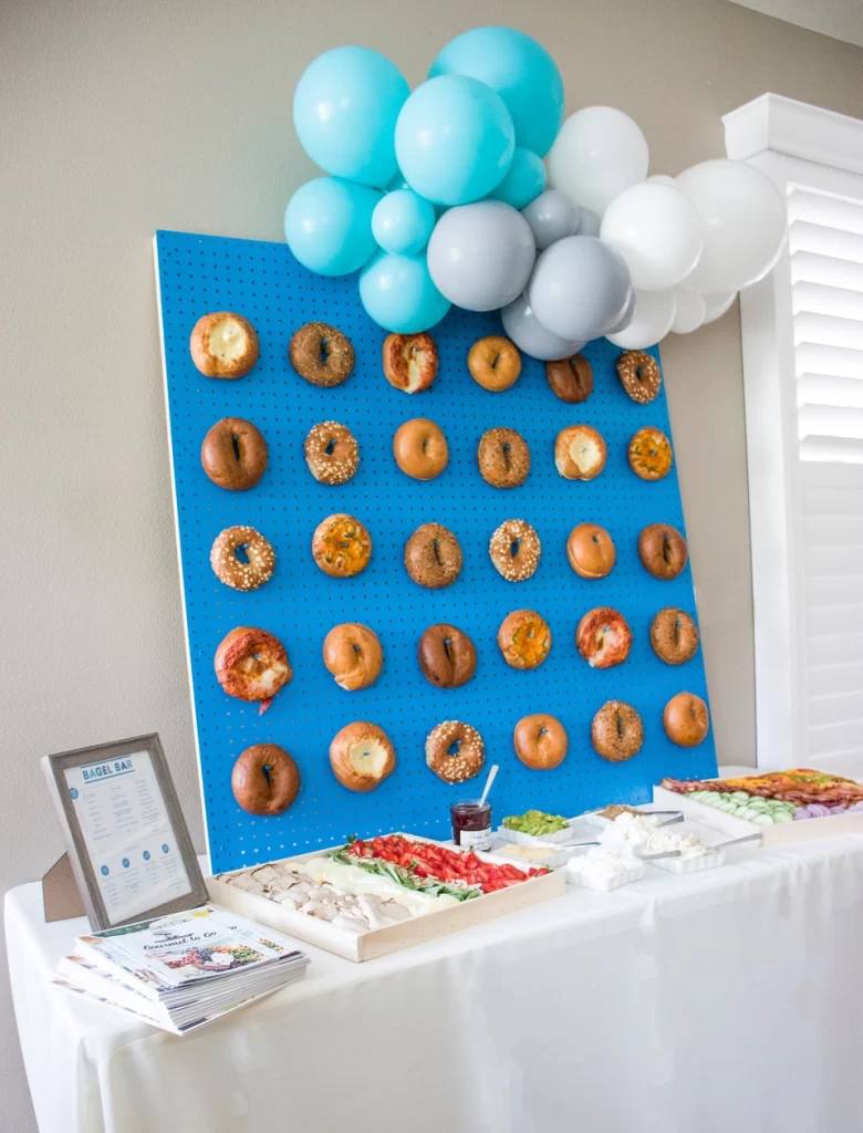 A blue peg board with bagels on it over a food table at a baby shower.