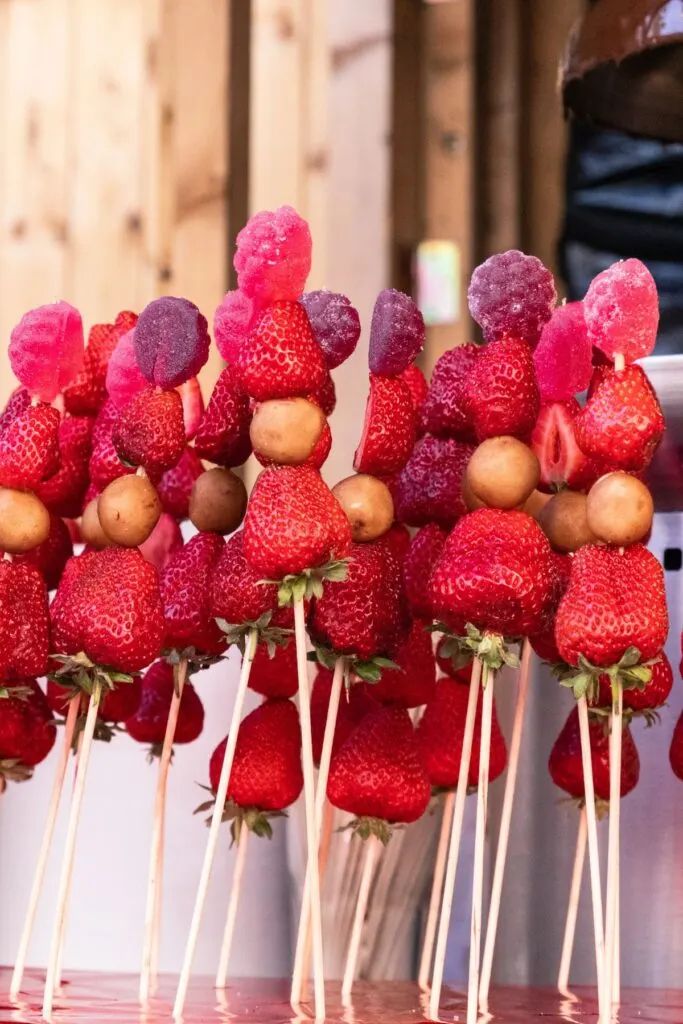 Several wooden skewers filled with pink and red fruits, including raspberries and strawberries.