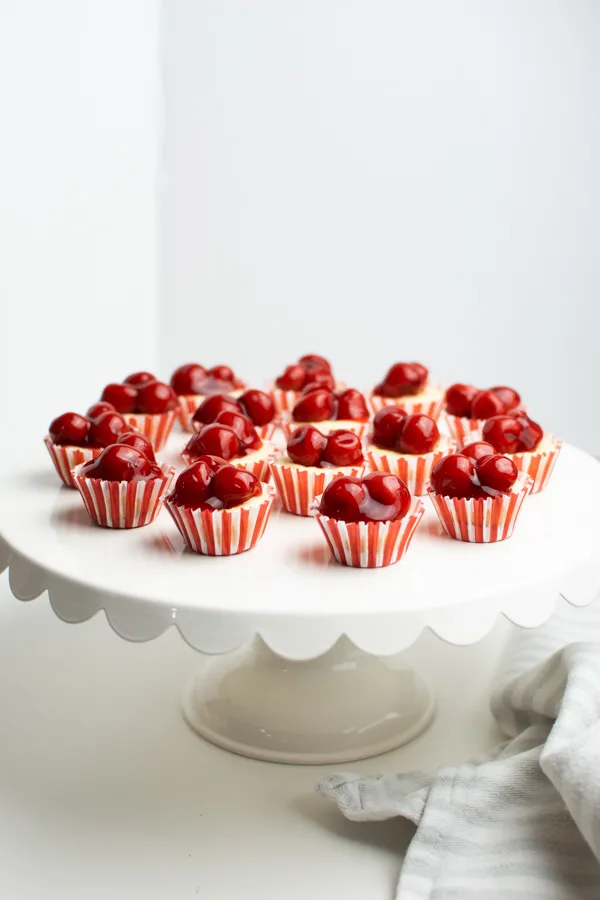 Mini cherry cheesecake bites on a white cake stand.