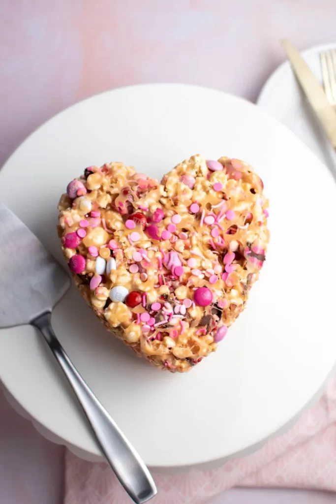 A heart-shaped caramel popcorn cake with pink and white candies.