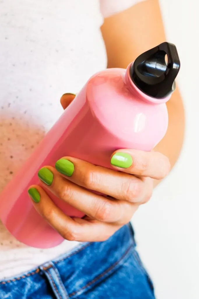 A woman with green painted fingernails holds a pink water bottle with a black top.
