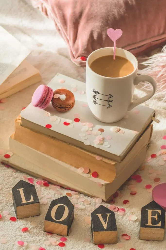 A coffee cup with cupid arrows sits on a stack of books next to blocks that spell the word "Love".