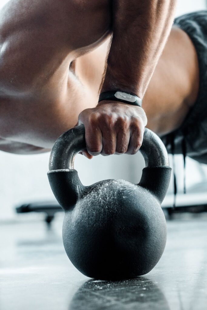 The torso and arm of a man doing push-ups on kettle bells.