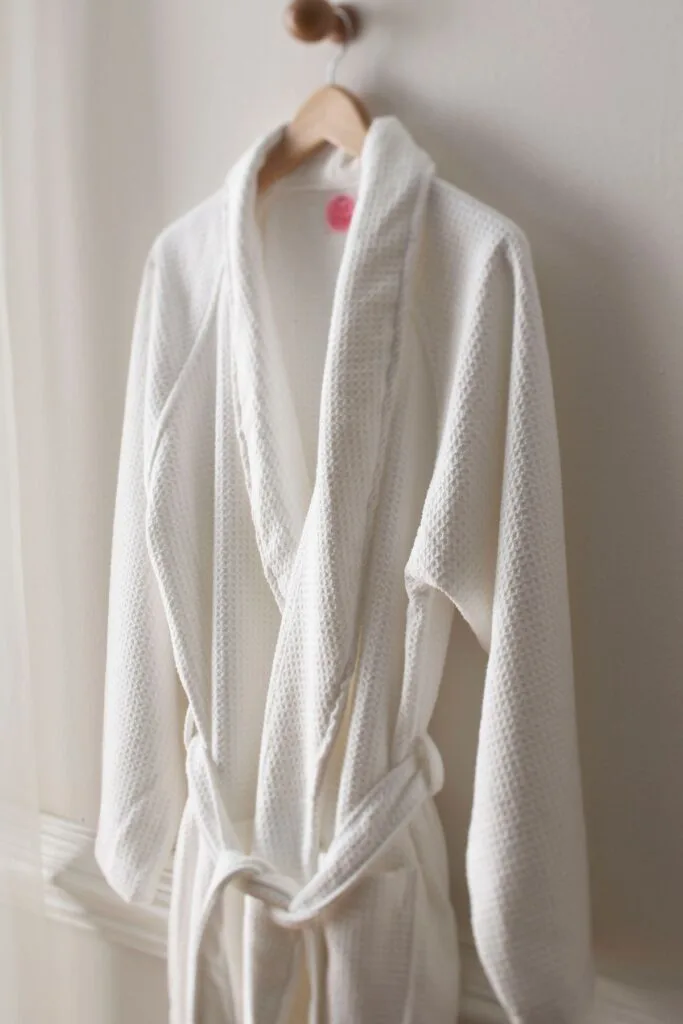 A plush white robe hangs from a hook on a white wall.