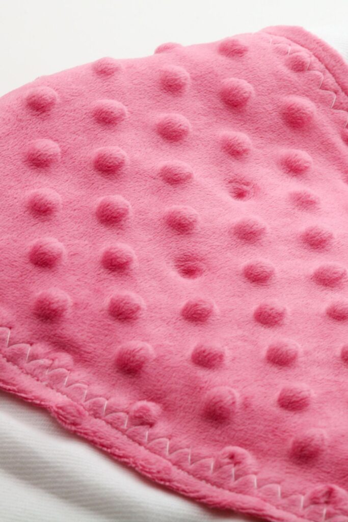 A pink baby blanket with bumps on a white background.